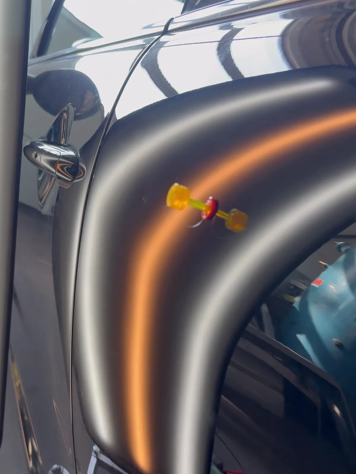 Klebeadapter mit Zugbrücke an einem schwarzen Kotflügel, die Delle zeichnet sich im Lichtband ab
